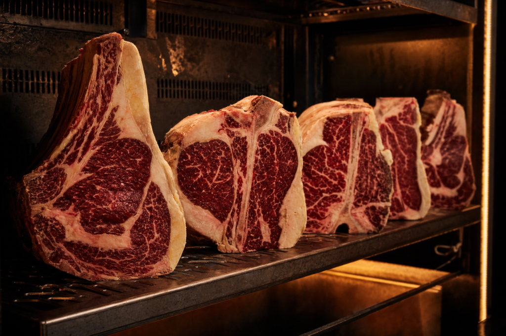 Bistecche di carne pregiata crude frollate Dry-Aged, allineate come in cella di frollatura
